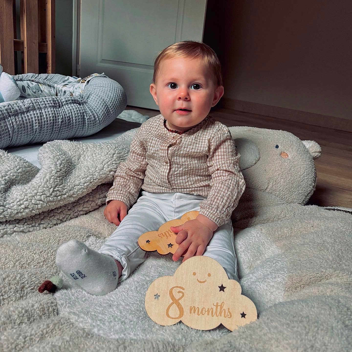 Eden a rejoint le concours — aidez-le/la à gagner de superbes lots ! 8_months, baby, blanket, child, clothing, cute, face, floor, head, indoors, infant, milestone, plush, portrait, sitting, smile, soft_lighting, toy, white_pants, wooden_toy
