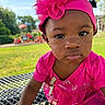 toddler, child, pink_dress, headband, flower, outdoor, playground, grass, table, metal_surface, face, expression, curious, sunlight, daylight, person, young_child, cute, close_up, summer