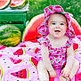 baby, blanket, child, colorful, cute, food, fruit, grass, green, happy, hat, nature, outdoor, patterned_clothing, pink, playful, sitting, smiling, summer, watermelon