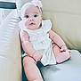 baby, child, infant, cute, sitting, white_dress, headband, flower, leather_couch, indoor, curious, chubby, skin, foot, hand, portrait, person, young, furniture, comfortable