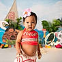 toddler, child, birthday, cake, flower, headband, red_clothing, smiling, indoor, celebration, moana_theme, decorations, colorful, cartoon_characters, background, plants, happy, portrait, party, one_year_old