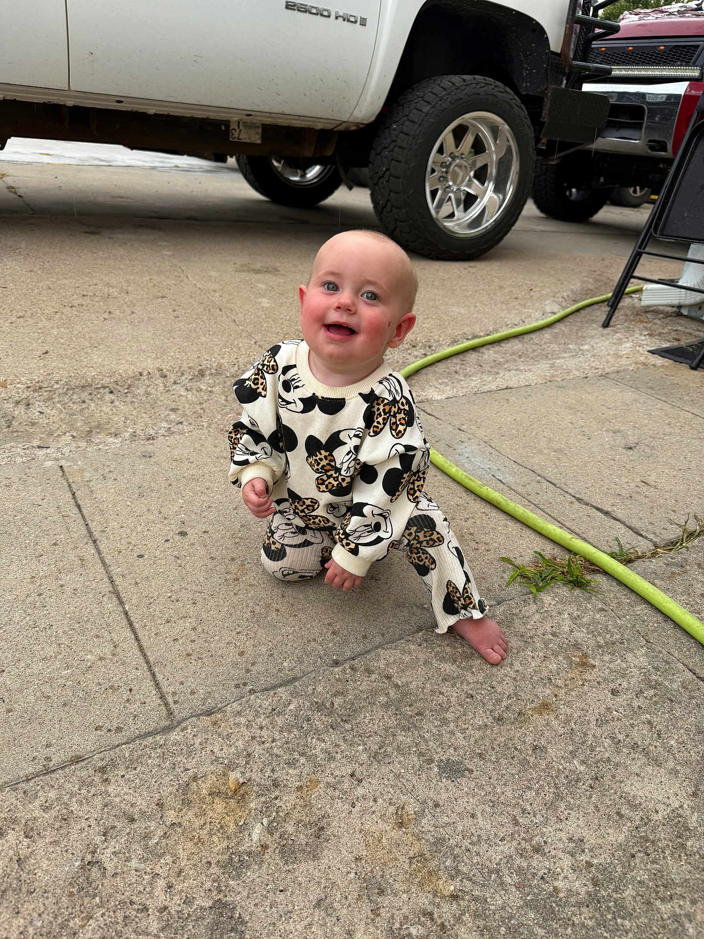 Oakley is registered to the contest to win money with this photo: baby, child, smiling, crouching, outdoor, concrete, truck, vehicle, hose, barefoot, clothing, cute, happy, person, face, head, playful, infant, daylight, casual