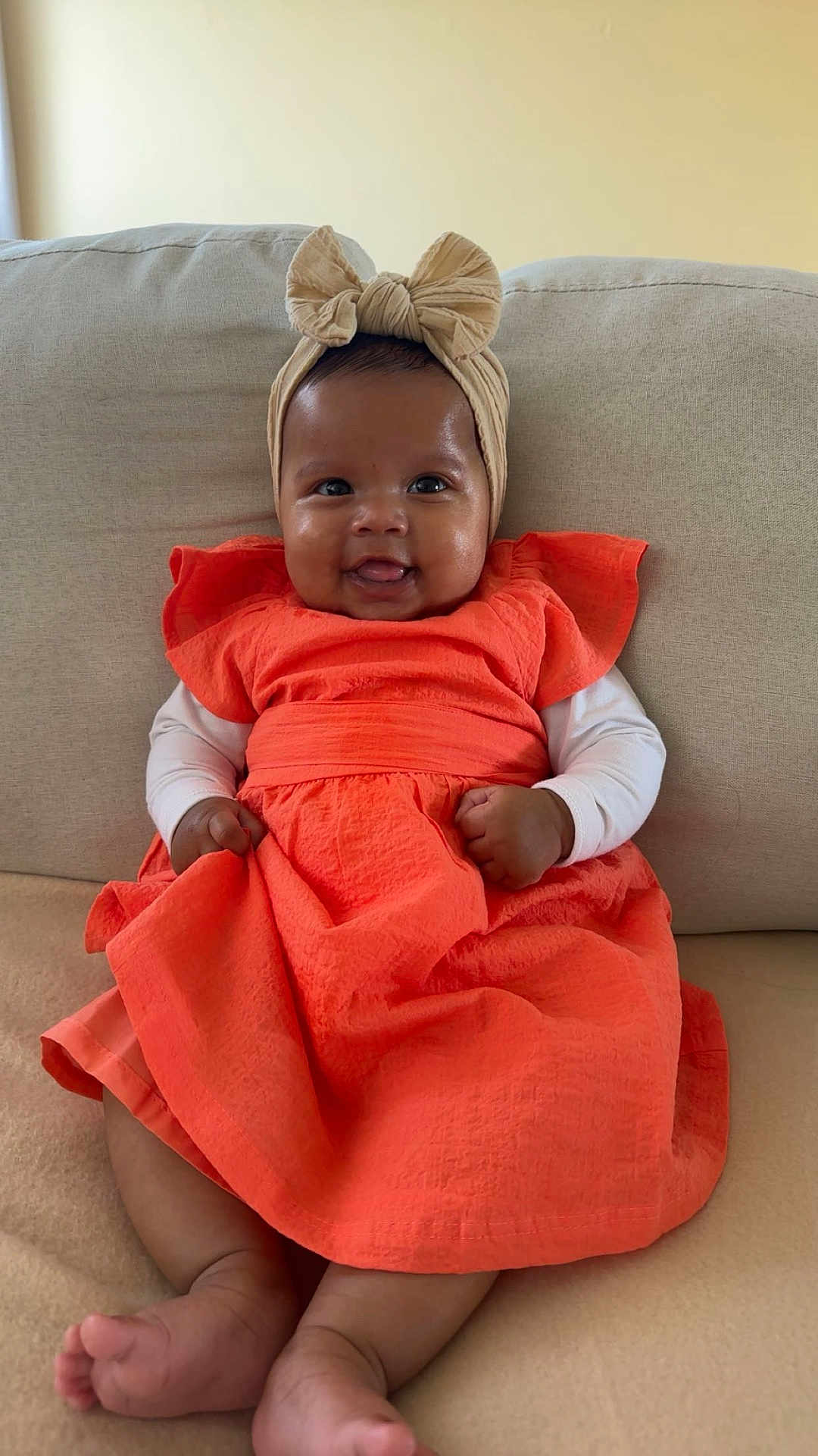 Neysta a rejoint le concours — aidez-le/la à gagner de superbes lots ! baby, child, smiling, orange_dress, headband, bow, couch, indoor, cute, happy, infant, person, sitting, furniture, skin, foot, hand, portrait, clothing, baby_fashion