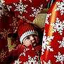 baby, child, face, red_hat, knit_hat, wrapping_paper, snowflake_pattern, holiday, christmas, curious_expression, indoors, cozy, festive, red_clothing, closeup, portrait, cute, winter, soft_light, surprise