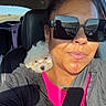 woman, puppy, dog, car, vehicle, selfie, sunglasses, seat_belt, highway, road_trip, portrait, fluffy, white_dog, passenger, driver, sunlight, outdoor, travel, pink_shirt, gray_jacket