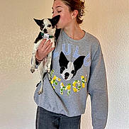 Honolulu is registered to the contest to win money with this photo: affection, black_and_white_dog, casual_clothing, cute, dog, dog_sweatshirt_design, earrings, gray_sweatshirt, holding, home, indoor, jeans, kiss, person, pet, portrait, short_hair, standing, textured_wall, wooden_floor