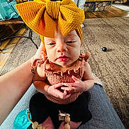 Eliza joined the competition — help win amazing prizes! baby, child, headband, bow, pacifier, indoor, carpet, hand, person, clothing, sitting, cute, infant, wooden_floor, tattoo, home, furniture, relaxing, cozy, casual