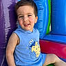 toddler, child, smiling, blue_clothing, sleeveless_shirt, cookie_monster, inflatable, playground, colorful, purple, blue, green, red, happy, sitting, indoor_play, fun, young_child, cute, portrait