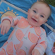 Lainey is registered to the contest to win money with this photo: baby, infant, smile, happy, onesie, orange_slice_pattern, blanket, grass, blue, playmat, portrait, face, cheek, eyes, hand, toy, lion_plush, outdoor, cute, laying_down