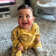 Ilyes a rejoint le concours — aidez-le/la à gagner de superbes lots ! baby, infant, toddler, smiling, sitting, yellow_clothing, patterned_socks, shaggy_carpet, indoor, living_room, television, shallow_depth_of_field, portrait, cute, happy, chubby_cheeks, playful, short_hair, onesie, cozy
