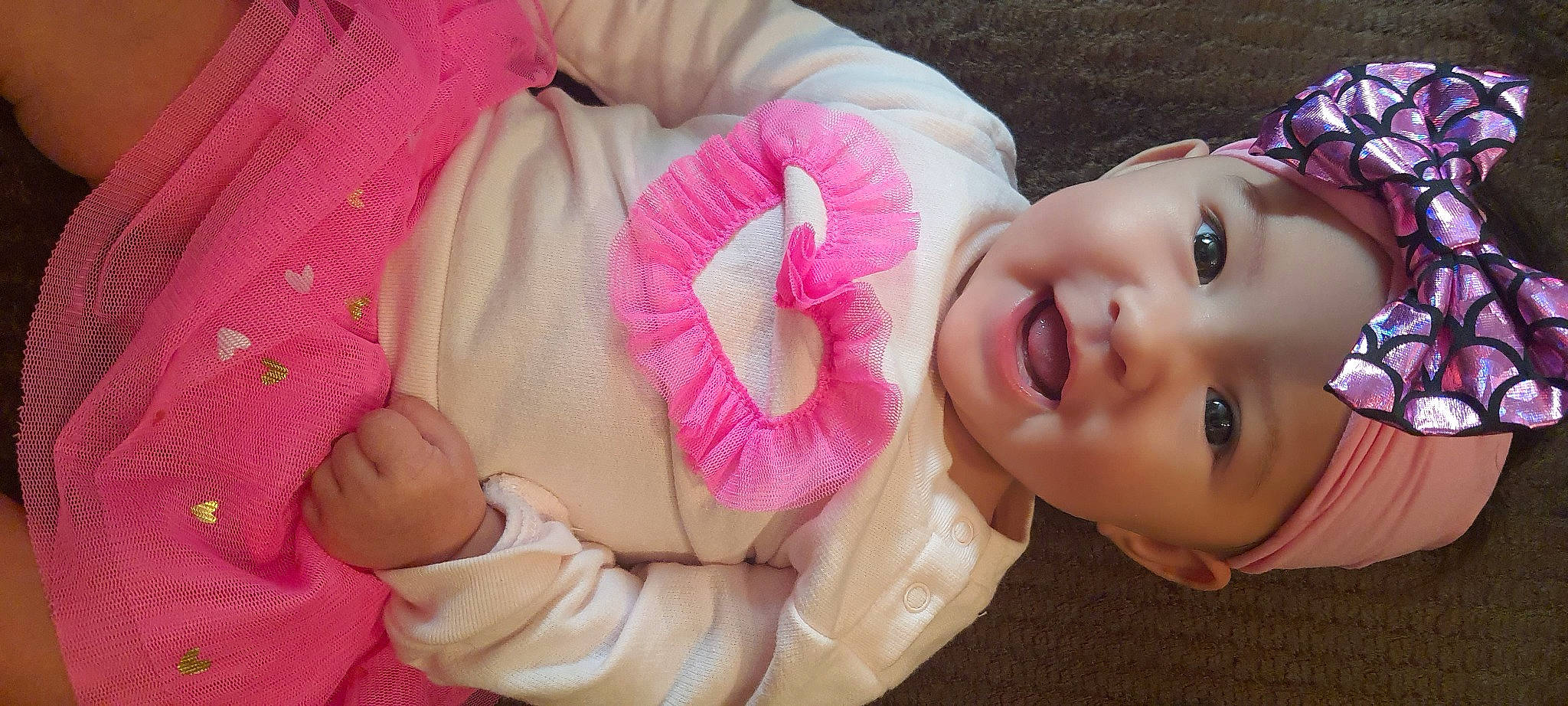 Kristine is registered to the contest to win money with this photo: arm, baby_toddler_clothing, cheek, eye, eyelash, face, finger, gesture, hand, happy, head, headwear, human_body, lip, mouth, nose, person, pink, plant, skin