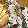 newborn, baby, infant, sleeping, onesie, mittens, dinosaur, person, hand, yellow_pajamas, hospital_wristband, blanket, floor, patterned_blanket, cozy, cute, indoor, holding, sleep, child