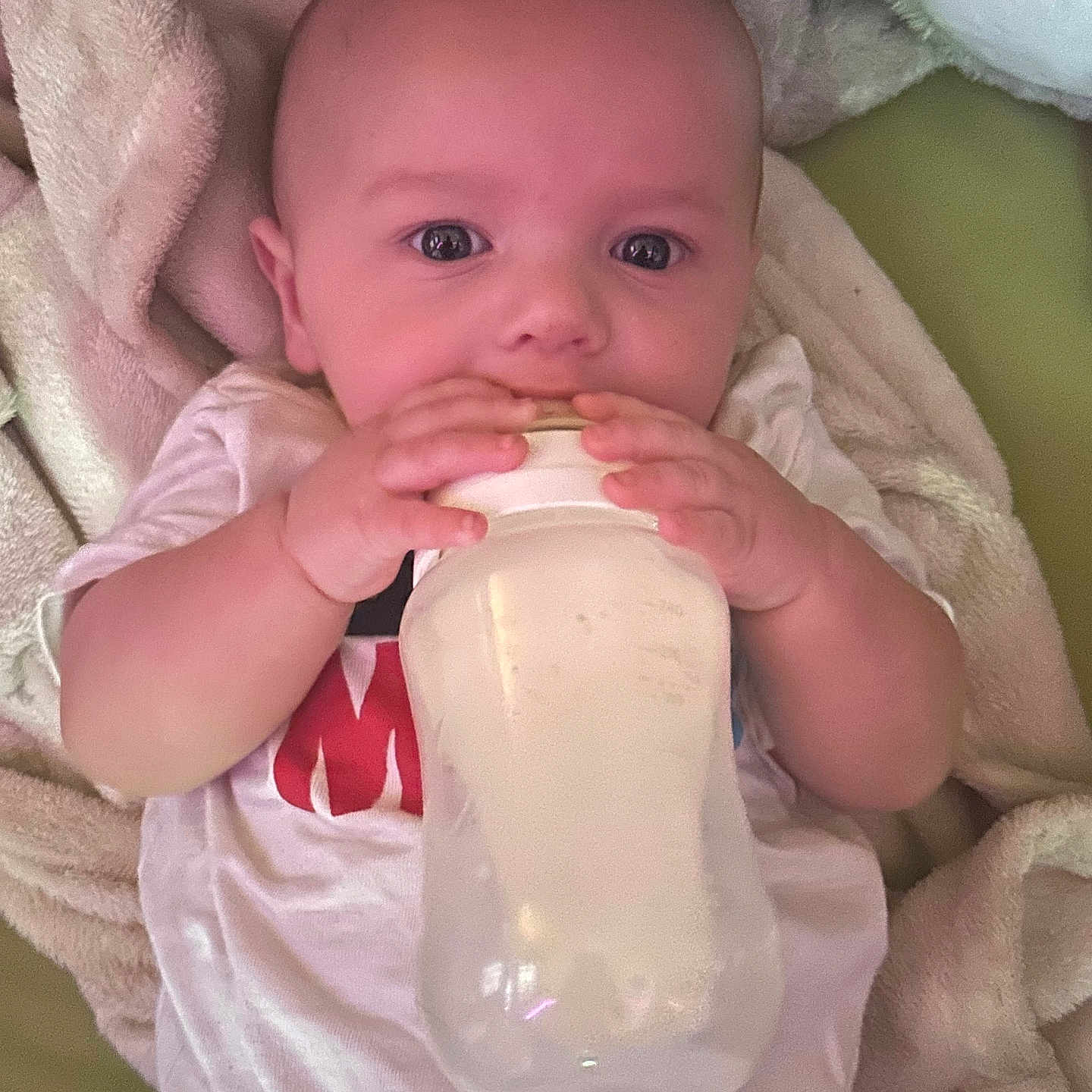 Elias joined the competition — help win amazing prizes! baby, bottle, milk, blanket, plush_toy, infant, hands, face, clothing, lying_down, cute, feeding, child, person, indoor, portrait, soft_texture, sleepwear, head, expression