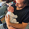 Elias joined the competition — help win amazing prizes! baby, newborn, man, holding, sleeping, indoor, casual_clothing, black_tshirt, blue_jeans, chair, table, glass, carpet, hand, face, arm, closeup, parent, love, comfort