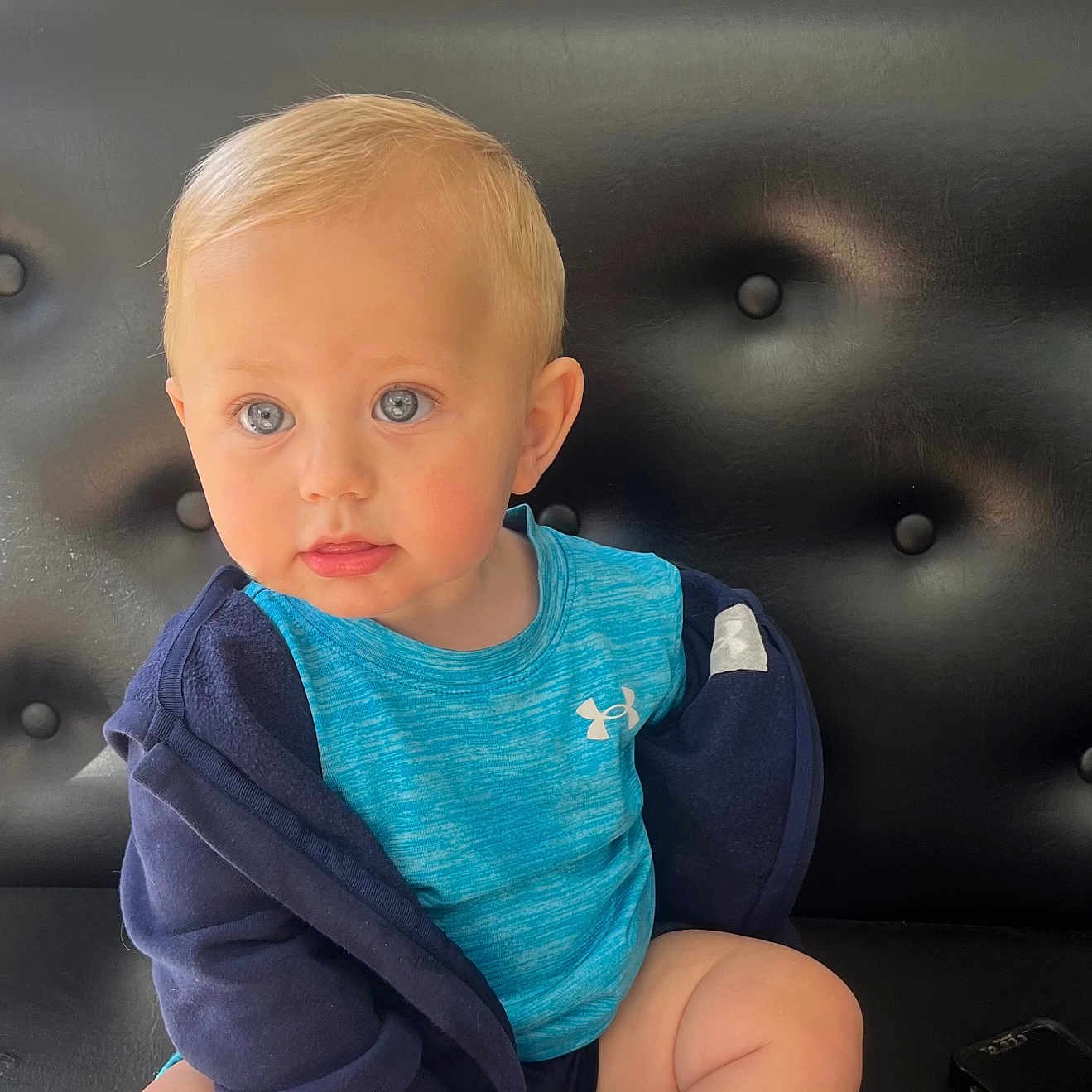Tommy is registered to the contest to win money with this photo: baby, black_couch, blue_eyes, blue_shirt, casual, child, clothing, curious, cute, footwear, hands, indoor, jacket, keys, legs, person, portrait, sitting, toddler, young_child