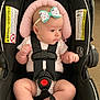 baby, infant, car_seat, headband, bow, safety_harness, warning_label, clothing, chubby, seated, curious, indoors, car_seat_strap, infant_clothing, child, cute, skin, person, seat, car