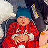 baby, baby_carrier, bear_hat, blanket, blue_hat, car_seat, child, cute, facial_expression, feet, hands, indoors, infant, plaid_outfit, plush_toy, portrait, red_clothing, sitting, stuffed_animal, wide_eyes