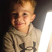 Lyncoln is registered to the contest to win money with this photo: child, smiling, hoodie, blond_hair, under_armour, indoor, portrait, light_source, happy, casual_clothing, young, cute, face, eyes, person, warm_lighting, dark_background, close_up, childhood, expression