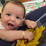 Kassidy joined the competition — help win amazing prizes! baby, infant, face, hand, pasta, penne, container, arm, bracelet, couch, fabric, home, indoor, expression, curly_hair, skin, smiling, closeup, person, cheerful