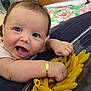 baby, infant, face, hand, pasta, penne, container, arm, bracelet, couch, fabric, home, indoor, expression, curly_hair, skin, smiling, closeup, person, cheerful