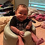 baby, infant, child, baby_seat, black_shirt, smile, indoor, window, blinds, blanket, bed, furniture, face, legs, feet, hand, expression, room, candid, person