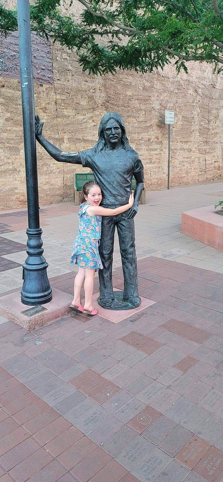 Ashtyn is registered to the contest to win money with this photo: art, child, clothing, flooring, fun, hairstyle, human_body, leg, leisure, monument, pedestrian, person, road_surface, sculpture, sidewalk, sitting, statue, street, temple, travel