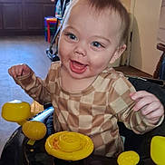 Chase is registered to the contest to win money with this photo: toddler, child, baby, walker, toy, yellow, black, checkered_shirt, smiling, happy, indoor, kitchen, furniture, floor, face, person, cute, playful, young_child, home