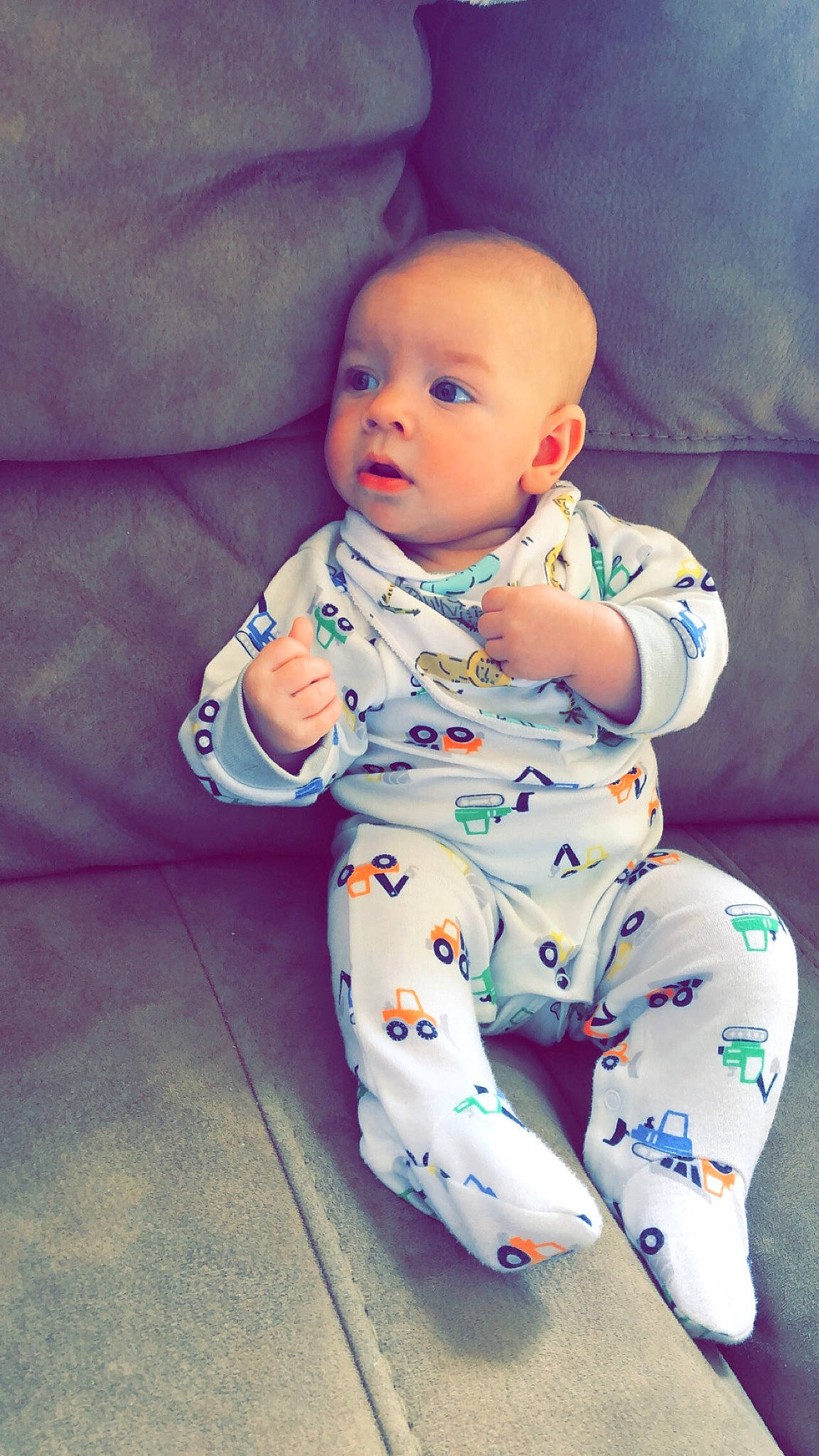 Maverick is registered to the contest to win money with this photo: baby, baby_toddler_clothing, child, comfort, cool, electric_blue, flooring, foot, happy, head, infant_bodysuit, knee, linens, pattern, person, sitting, skin, sleeve, t_shirt, textile