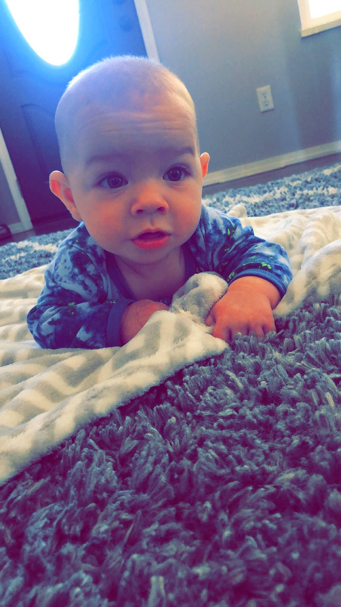 Maverick is registered to the contest to win money with this photo: azure, baby, baby_toddler_clothing, beauty, blue, child, cloud, comfort, electric_blue, finger, flooring, head, linens, mammal, person, purple, skin, textile, toddler, tummy_time