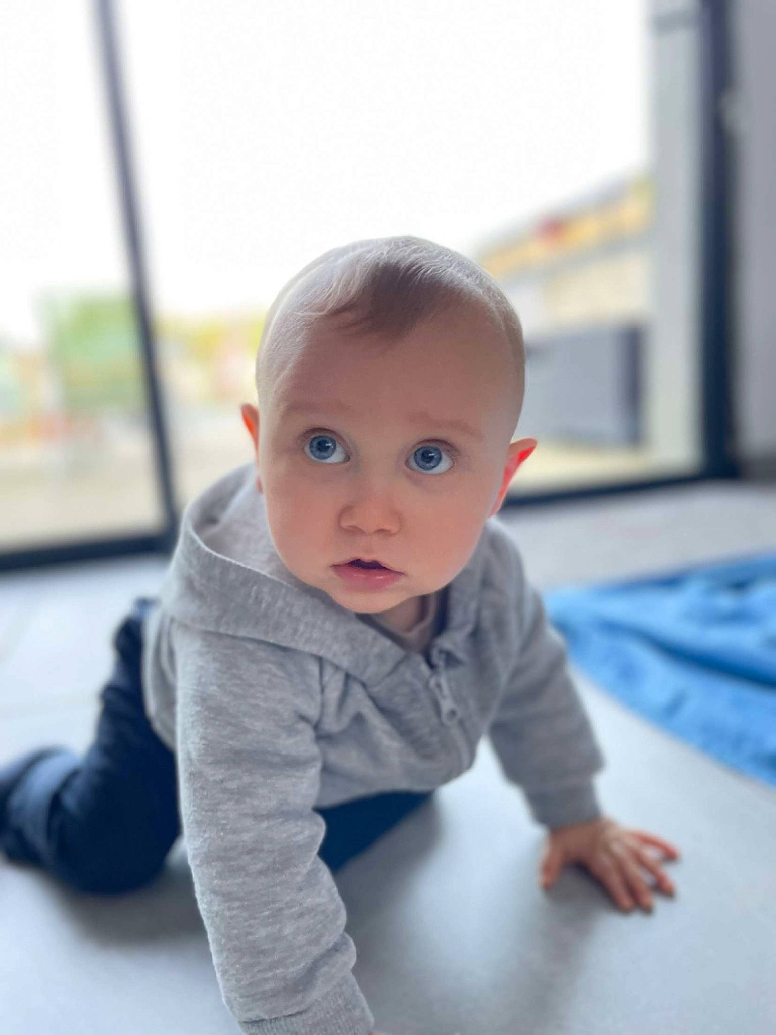 Louka participe au concours pour gagner de l'argent avec cette photo : baby, baby_toddler_clothing, cheek, child, comfort, electric_blue, eye, flooring, fun, grey, happy, hardwood, human_body, person, portrait_photography, room, sitting, skin, sleeve, surprise