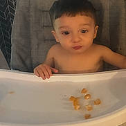 Kobe is registered to the contest to win money with this photo: child, toddler, baby, high_chair, sitting, shirtless, face, pouting, short_hair, indoor, home, kitchen, tray, food, snacks, crumbs, chair, portrait, phone_screenshot, warm_lighting