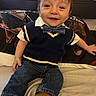 child, toddler, smiling, portrait, indoor, sitting, bed, bedding, bow_tie, sweater_vest, shirt, jeans, boots, brown_hair, face, happy, baby, furniture, warm_lighting, home