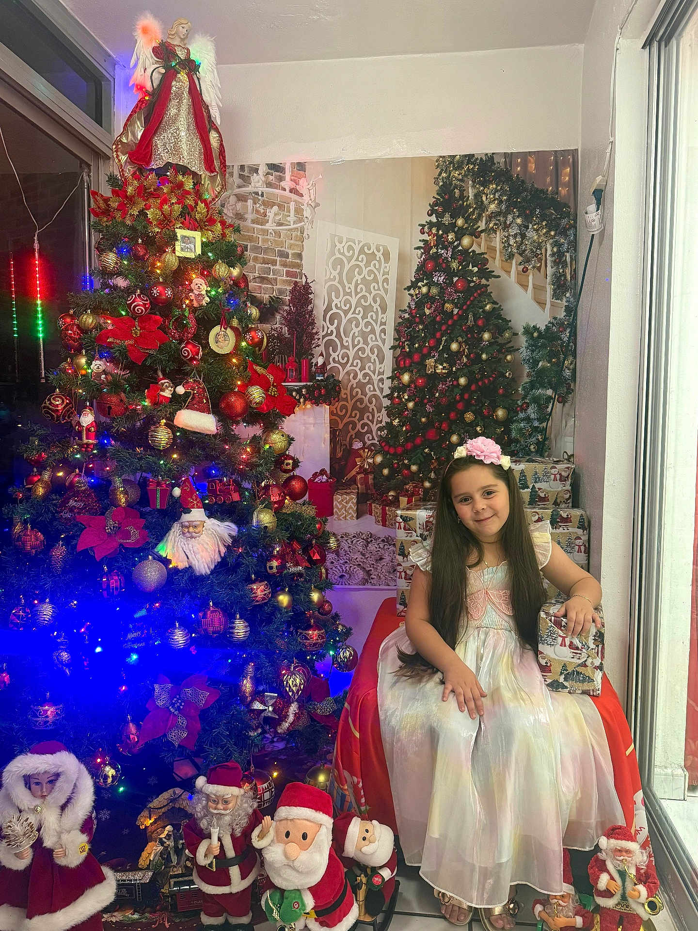 Nathaly Roque joined the competition — help win amazing prizes! child, girl, christmas_tree, holiday_decorations, santa_claus, gift_box, dress, flower_headband, indoor, festive, smiling, long_hair, floor, window, lights, ornaments, holiday, celebration, seasonal, decor