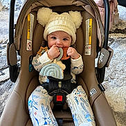 Anya is registered to the contest to win money with this photo: baby, infant, child, car_seat, beanie_hat, pom_poms, teether, plush_toy, onesie, patterned_clothing, five_point_harness, buckle, safety_warning_label, stroller_handle, rug, backpack, indoor, smiling, chewing, cozy