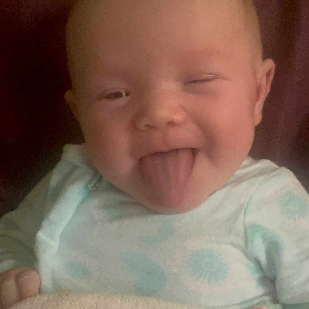 Aaliyah Smith is registered to the contest to win money with this photo: baby, infant, child, portrait, face, winking, tongue_out, smiling, happy, sitting, blanket, onesie, clothing, cozy, curtain, indoors, close_up, head, cute, photography