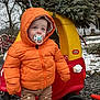toddler, child, orange_jacket, pacifier, toy_car, christmas_tree, winter, snow, boots, outdoor, play, cold_weather, tree, pants, cute, holiday, nature, clothing, person, seasonal