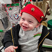 Kaleb joined the competition — help win amazing prizes! toddler, child, smiling, shopping_cart, headband, reindeer_antlers, jingle_bells, holiday, christmas, store, aisle, clothing, grey_sweatshirt, black_jacket, face, happy, indoor, person, cute, festive