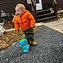 toddler, child, orange_jacket, laughing, toy, dinosaur, bubble_machine, outdoor, pavement, leaves, house, stairs, boots, camouflage_pants, statue, grass, play, happy, person, daylight