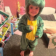 Danni joined the competition — help win amazing prizes! child, dinosaur_costume, barefoot, smile, indoor, carpet, toy_shelf, bedroom, childrens_room, plush_toy, pink_wall, furniture, playroom, young_child, cute, costume, person, feet, curly_hair, happy