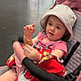 Danni is registered to the contest to win money with this photo: baby, blanket, casual, child, curious, expression, face, floor, glass_door, hand, hat, headwear, indoor, person, pink_clothing, resting, seat_belt, snack, stroller, toddler