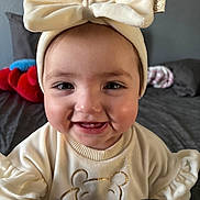 Amaralyn is registered to the contest to win money with this photo: baby, bed, blanket, bow_headband, cheeks, child, close_up, clothing, cute, eyes, face, happy, headband, indoors, infant, plush_toy, portrait, smiling, sweater, teeth