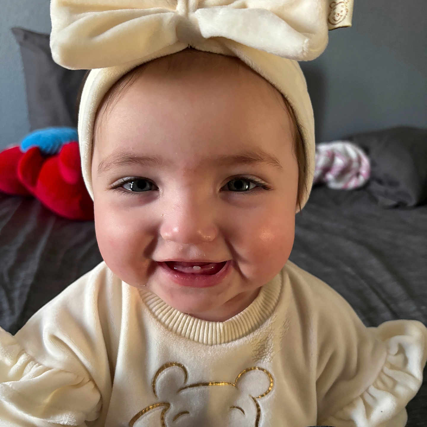 Amaralyn is registered to the contest to win money with this photo: baby, bed, blanket, bow_headband, cheeks, child, close_up, clothing, cute, eyes, face, happy, headband, indoors, infant, plush_toy, portrait, smiling, sweater, teeth