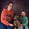 Roc participe au concours pour gagner de l'argent avec cette photo : german_shepherd, dog, woman, child, family, portrait, smiling, sitting, indoor, studio, textured_background, orange_hoodie, green_hoodie, sunglasses, eyeglasses, tongue_out, pet, companion_animal, chairs, casual_clothing