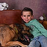 boy, child, dog, belgian_malinois, pet, portrait, smiling, sitting, couch, leather_sofa, hoodie, jeans, flowers, roses, indoor, studio, brown_dog, green_clothing, animal_companion, happy