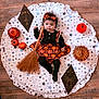 baby, black_clothing, blanket, broom, costume, cute, decorations, festive, floor, halloween, headband, holiday, indoors, infant, lying_down, orange_clothing, person, portrait, pumpkin, stars