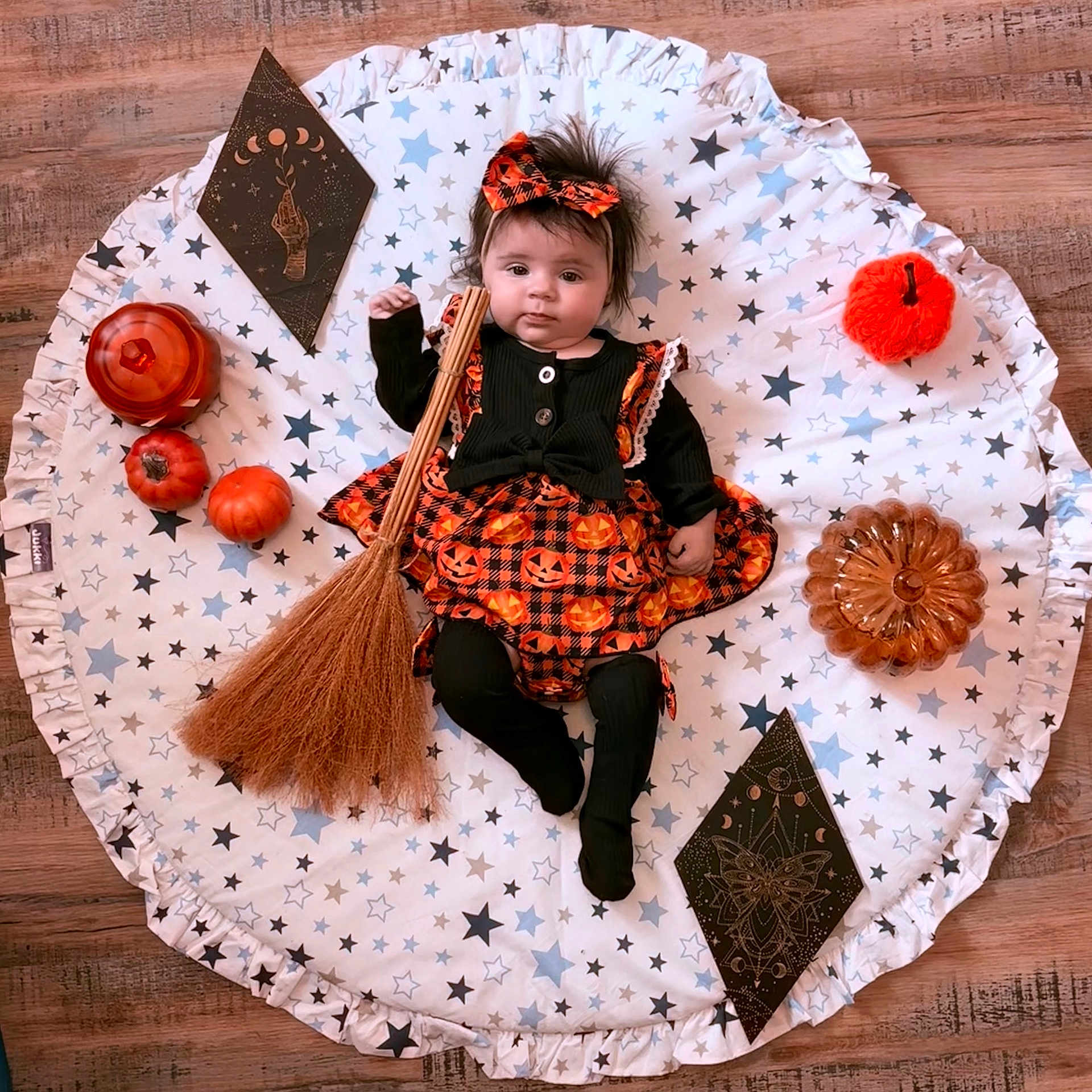 Charlotte participe au concours pour gagner de l'argent avec cette photo : baby, black_clothing, blanket, broom, costume, cute, decorations, festive, floor, halloween, headband, holiday, indoors, infant, lying_down, orange_clothing, person, portrait, pumpkin, stars