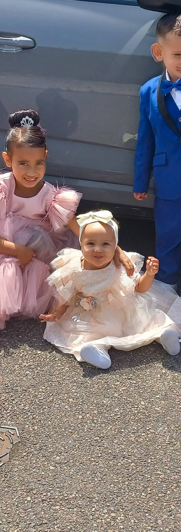 Inaya participe au concours pour gagner de l'argent avec cette photo : baby, baby_toddler_clothing, bridal_accessory, bridal_clothing, ceremony, child, dress, event, face, facial_expression, formal_wear, fun, gesture, grass, hairstyle, happy, headwear, joy, person, sitting