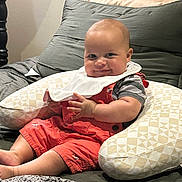 William joined the competition — help win amazing prizes! baby, infant, smile, red_overalls, bib, pillow, bed, blanket, cushion, indoor, child, cute, happy, person, skin, head, hand, legs, clothing, relaxing