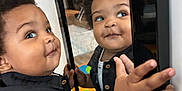 Omari is registered to the contest to win money with this photo: baby, black_shirt, child, colorful, curious, curly_hair, cute, expression, face, hand, home, indoor, mirror, person, playmat, portrait, reflection, smile, toddler, young_child