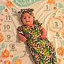 baby, infant, milestone_blanket, months, headband, cactus_pattern, leopard_print, floral, ring_marker, lying_down, portrait, smile, face, hand, fabric, cozy, patterned_clothing, nursery, warm_lighting, cute